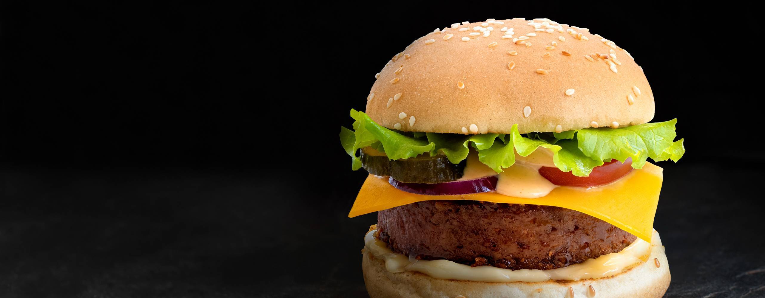 Växtbaserad burgare i bröd med sesamfrön med sallad och ost på svart bakgrund.