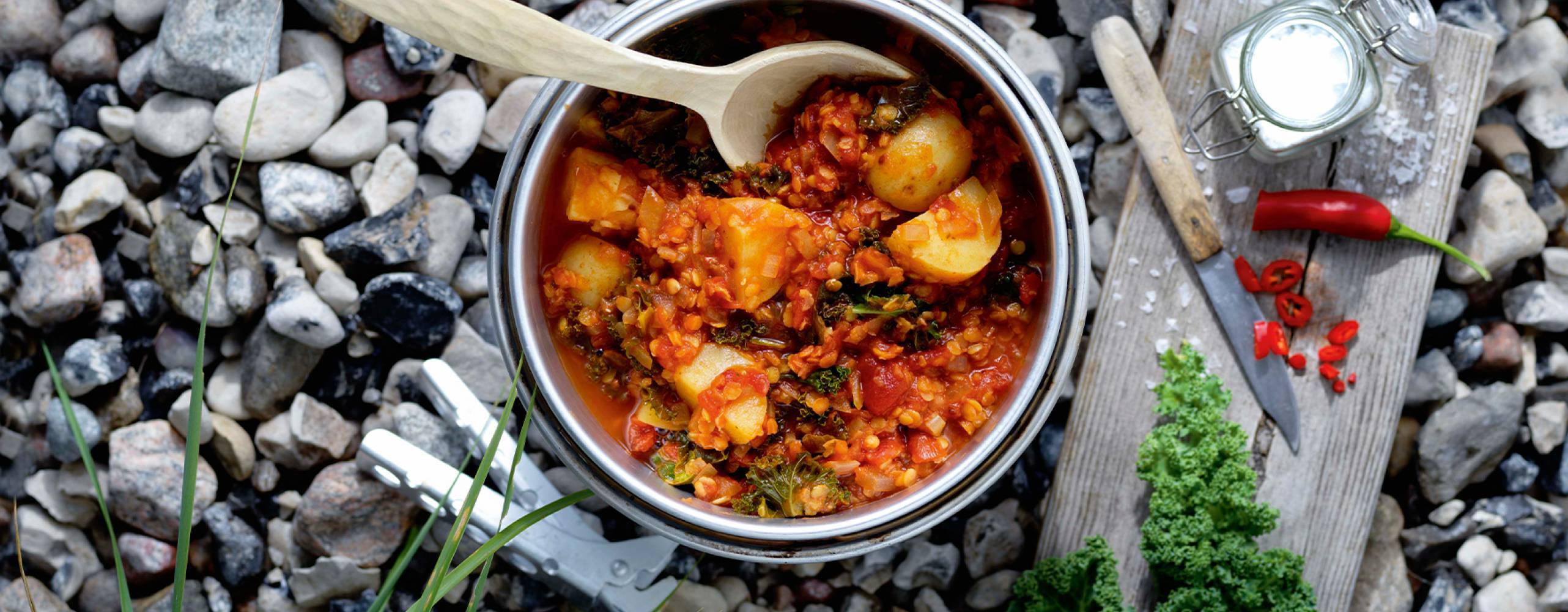 Foto: Ulrika Pousette Potatis one pot i en gryta på småstenar med en träbräda med en kniv, röd chili och flingsalt bredvid