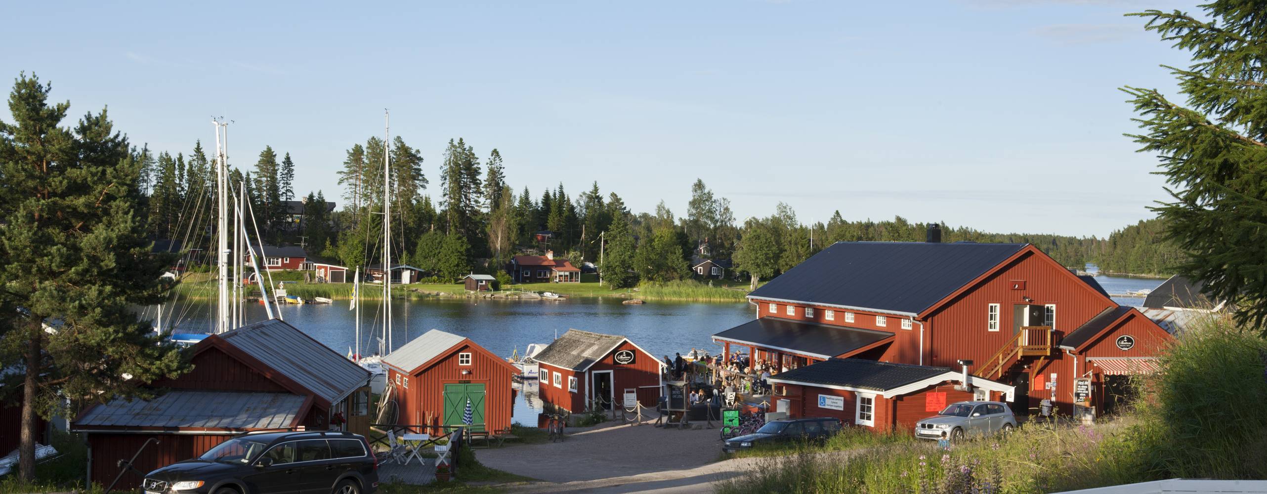 Foto: Scandphoto/Shutterstock View of several red buildings in evening lit on July 17, 2012 in Jungfrukusten, Sweden. Gravel road, wooden fence, bridge and a Restaurant.