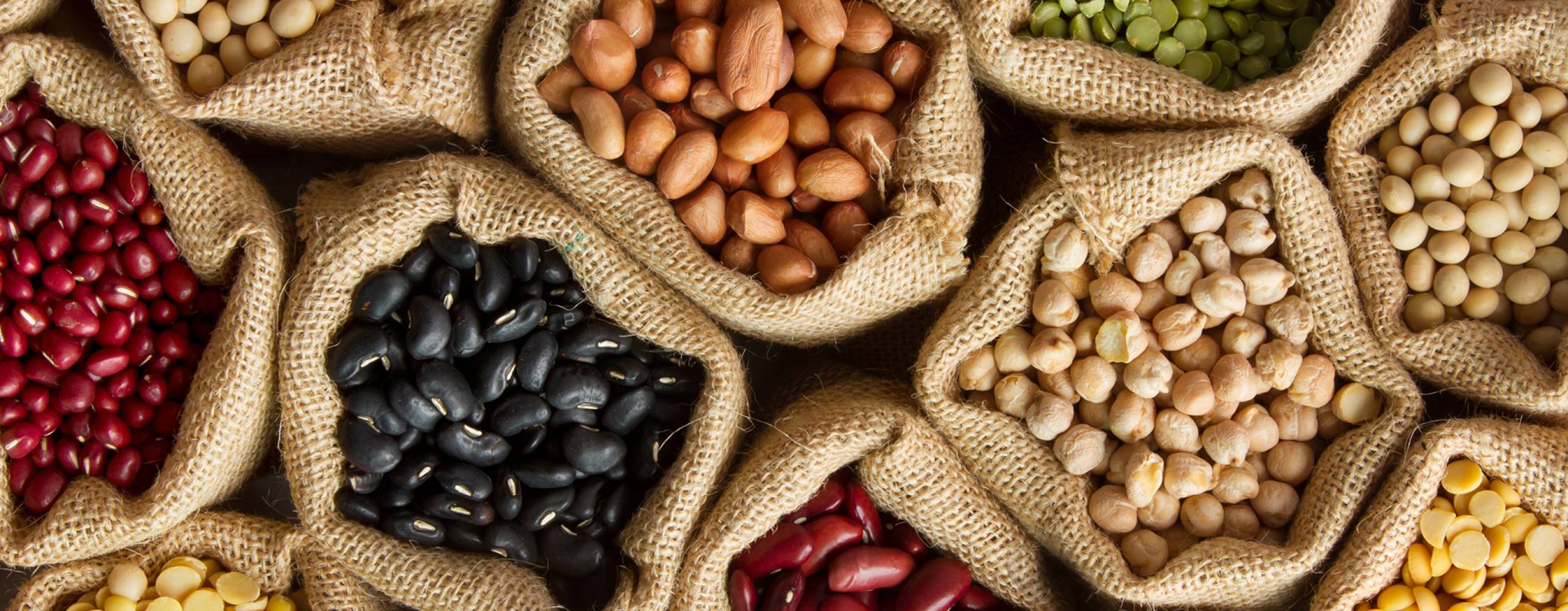 Många olika färgglada baljväxter i påsar av säckväv, fotade ovanifrån.