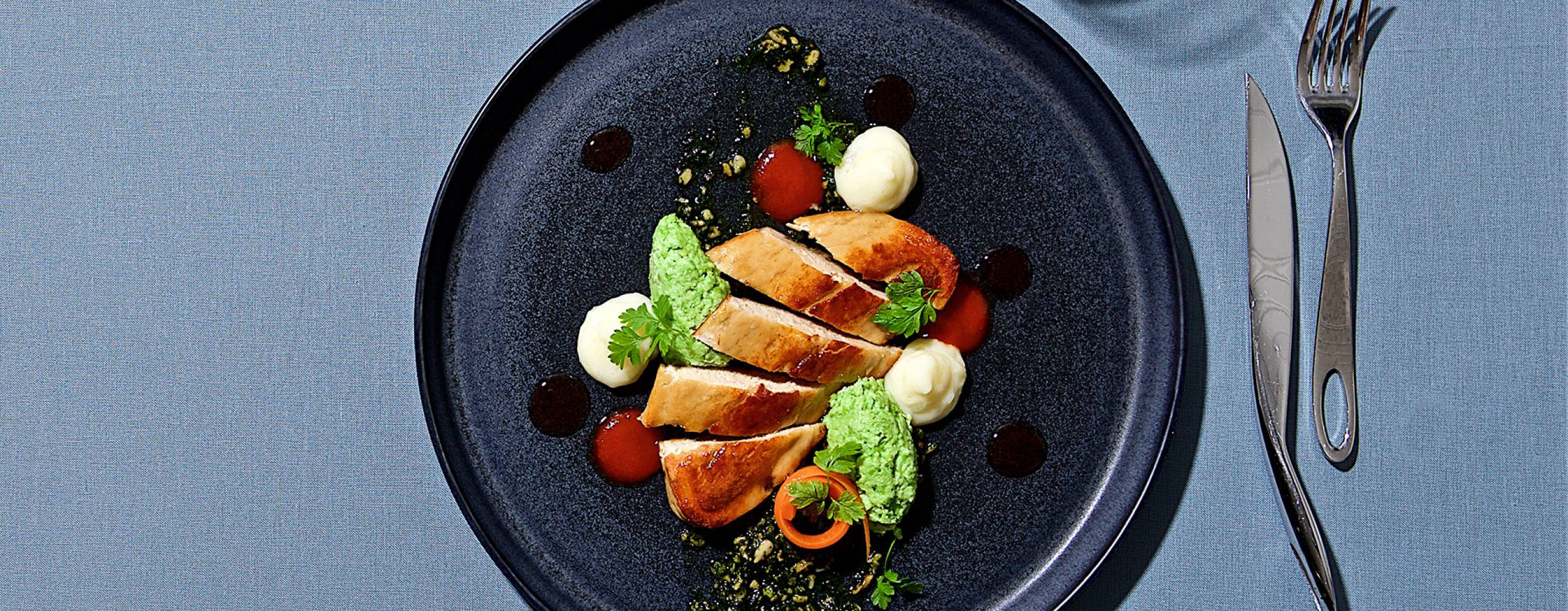 Vegansk quornfilé på tallrik med bestick och vattenglas runtom, fotat ovanifrån mot blå bakgrund.