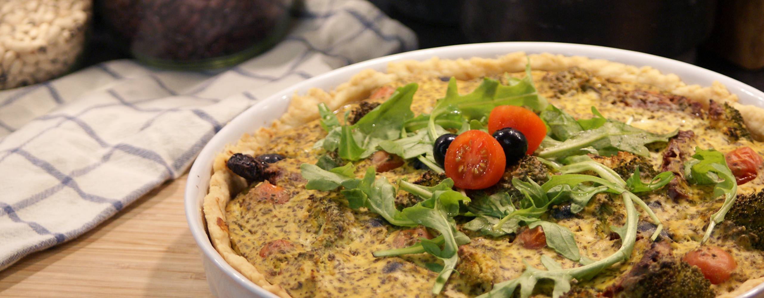 Nygräddad matpaj i vit pajform, ståendes på en skärbräda av trä. Bredvid ligger en rutig kökshandhud.