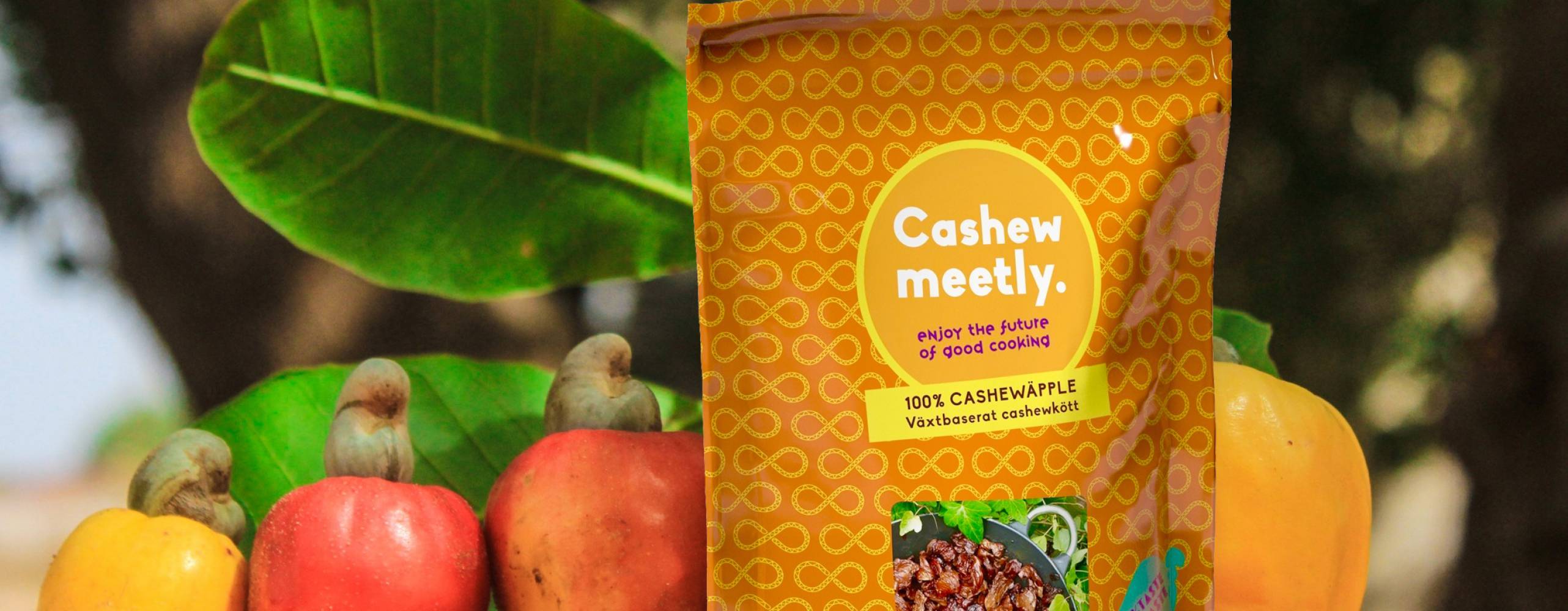 Foto: Axfood/Cashewmeetly Cashewmeetly i förpackning med cashewäpplen och grönska i bakgrunden.