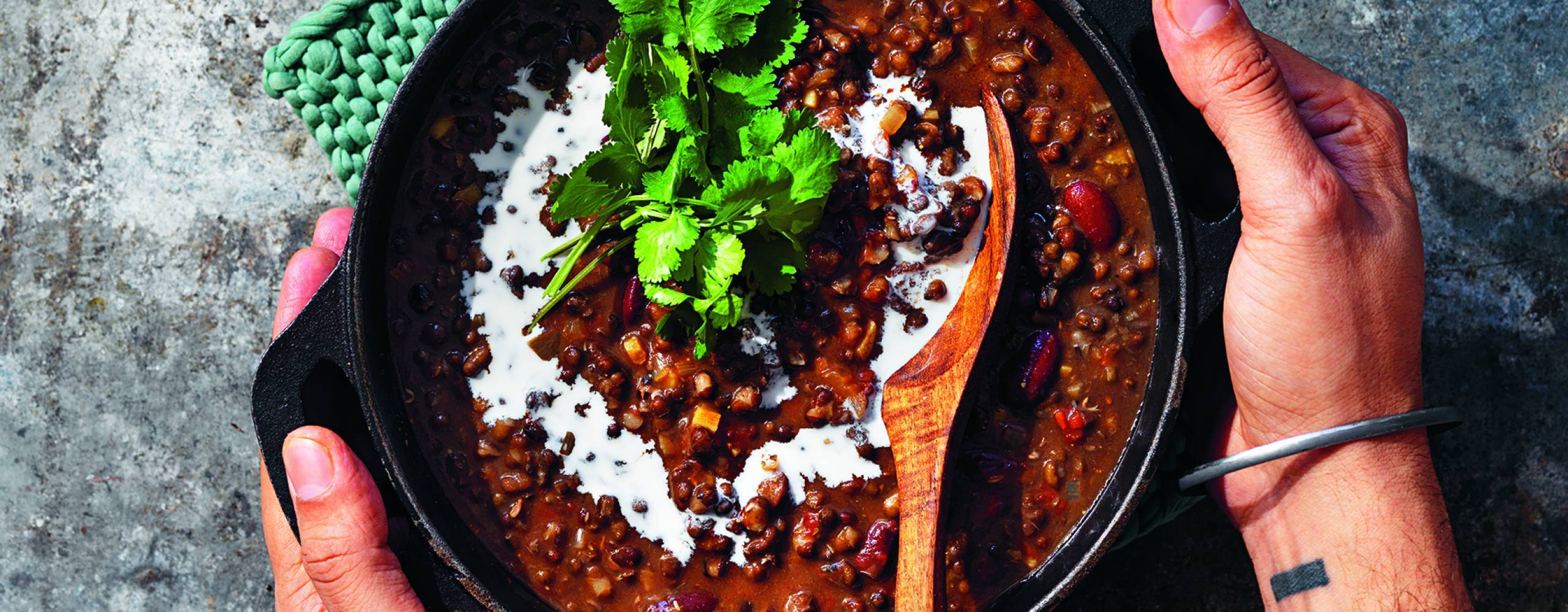 Dal makhani i gryta på bord. Två händer håller om grytan.