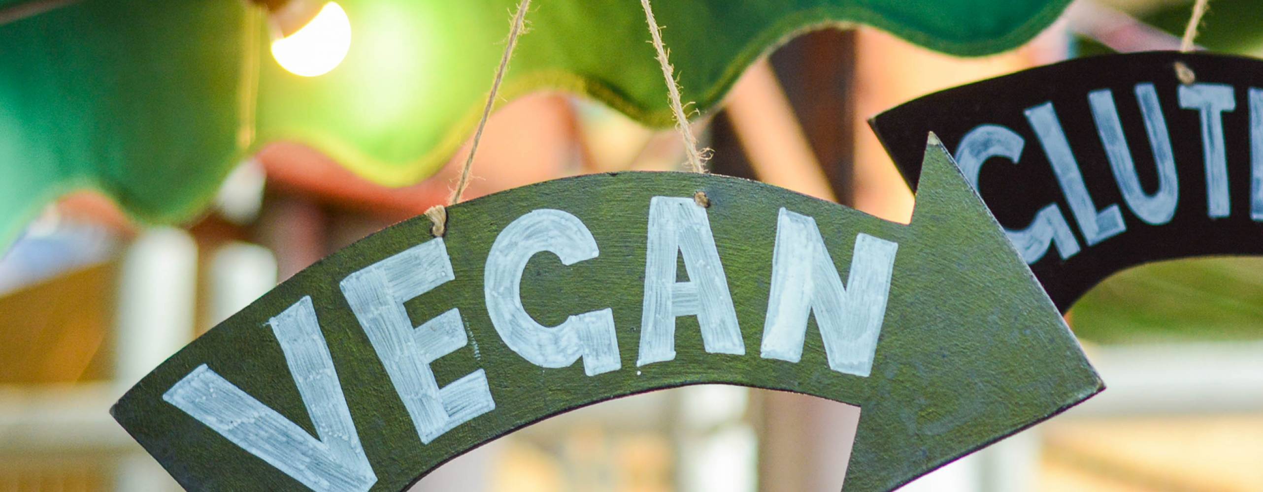 Pilformad skylt med texten "vegan", hängandes från ett parasol i dovt upplyst miljö.