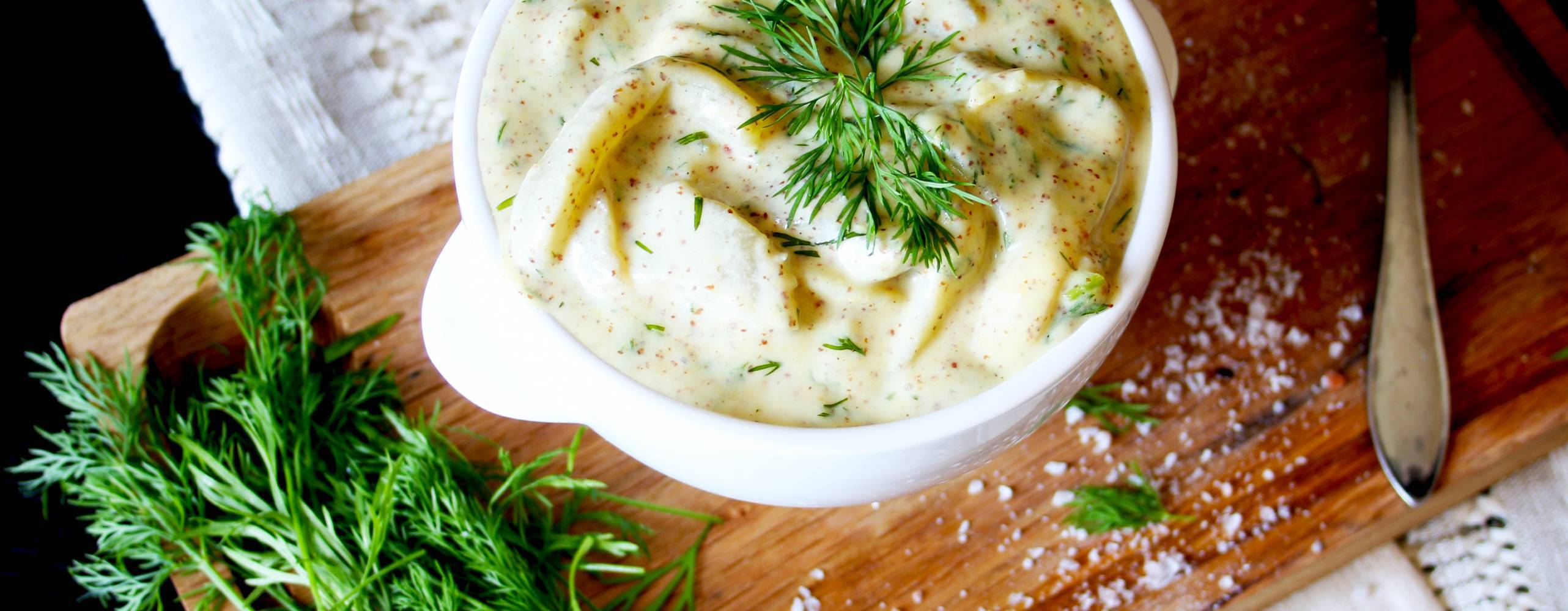 Auberginesill i senap i en skål på skärbräda av trä, med färsk dill vid sidan av.