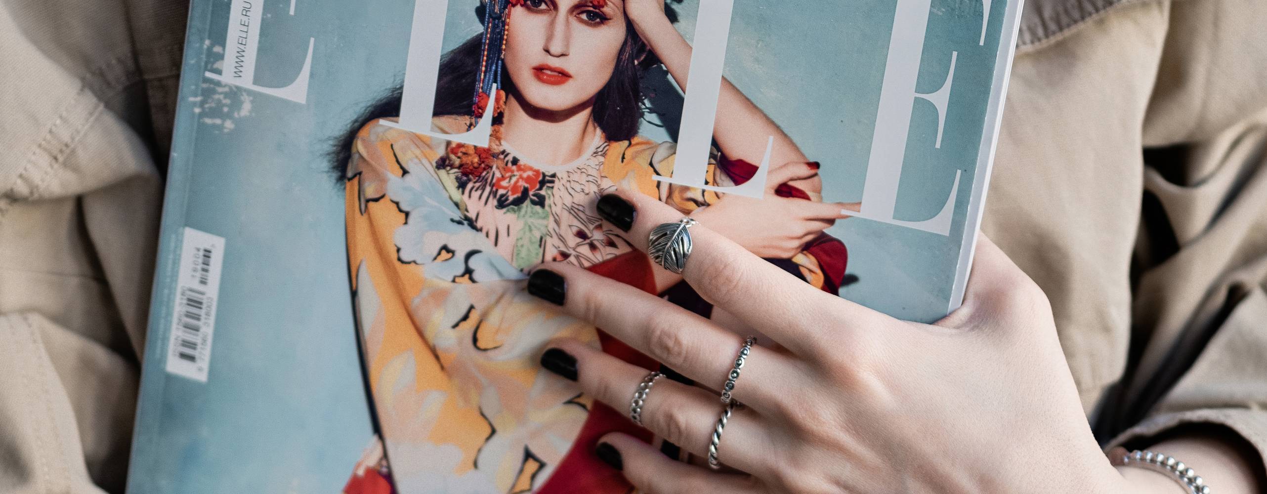 Person iklädd beige jacka håller i ett exemplar av ELLE magazine