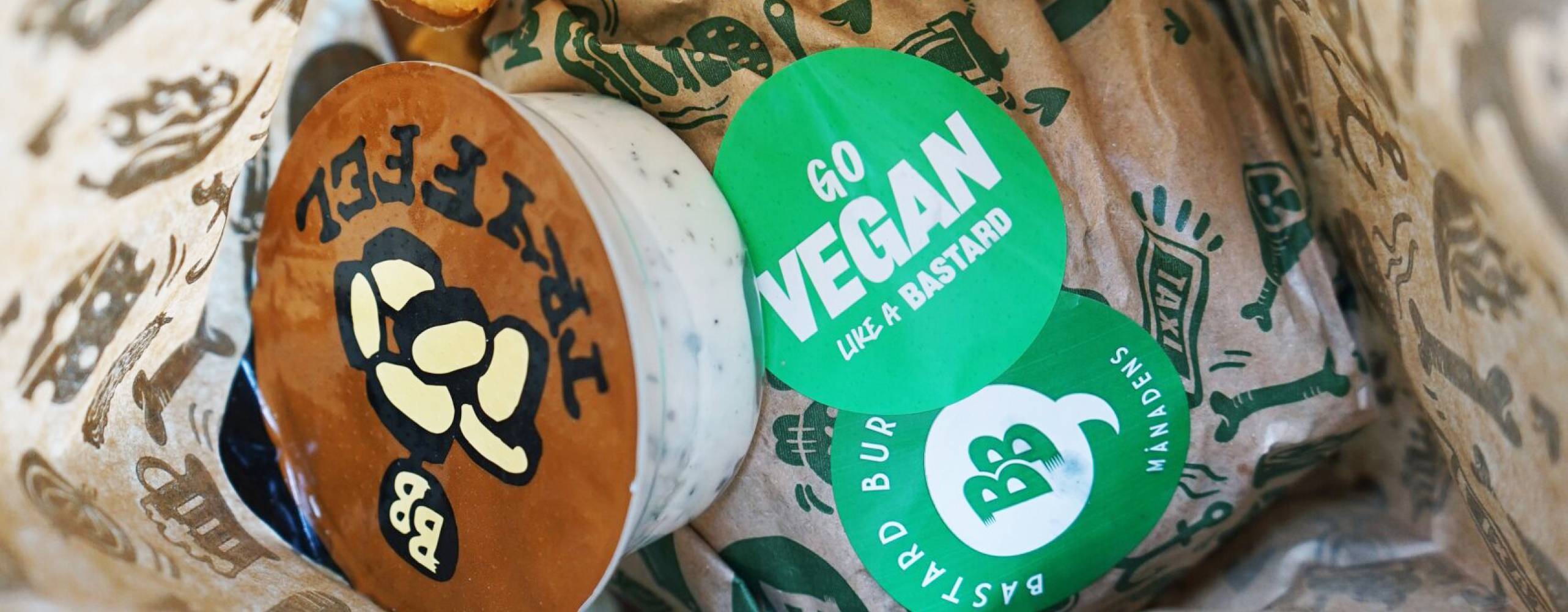 Burgare, pommes och sås från Bastard Burgers i papperspåse. På burgaren finns ett klistermärke med texten &quot;Go vegan like a bastard&quot;.