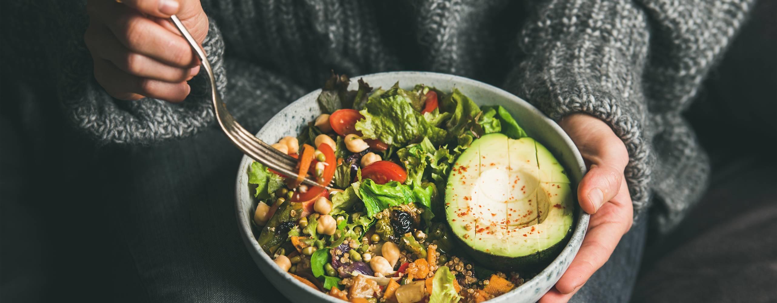 Kvinna sitter med skål med matig sallad i knäet.