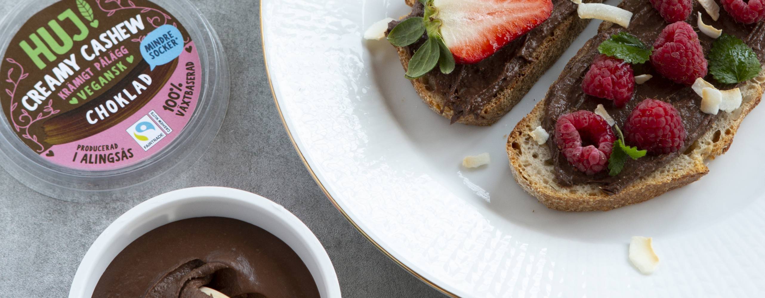 HUJ Creamy Cashew Choklad i öppnad förpackning till vänster. Till höger på macka med bär och kokos.