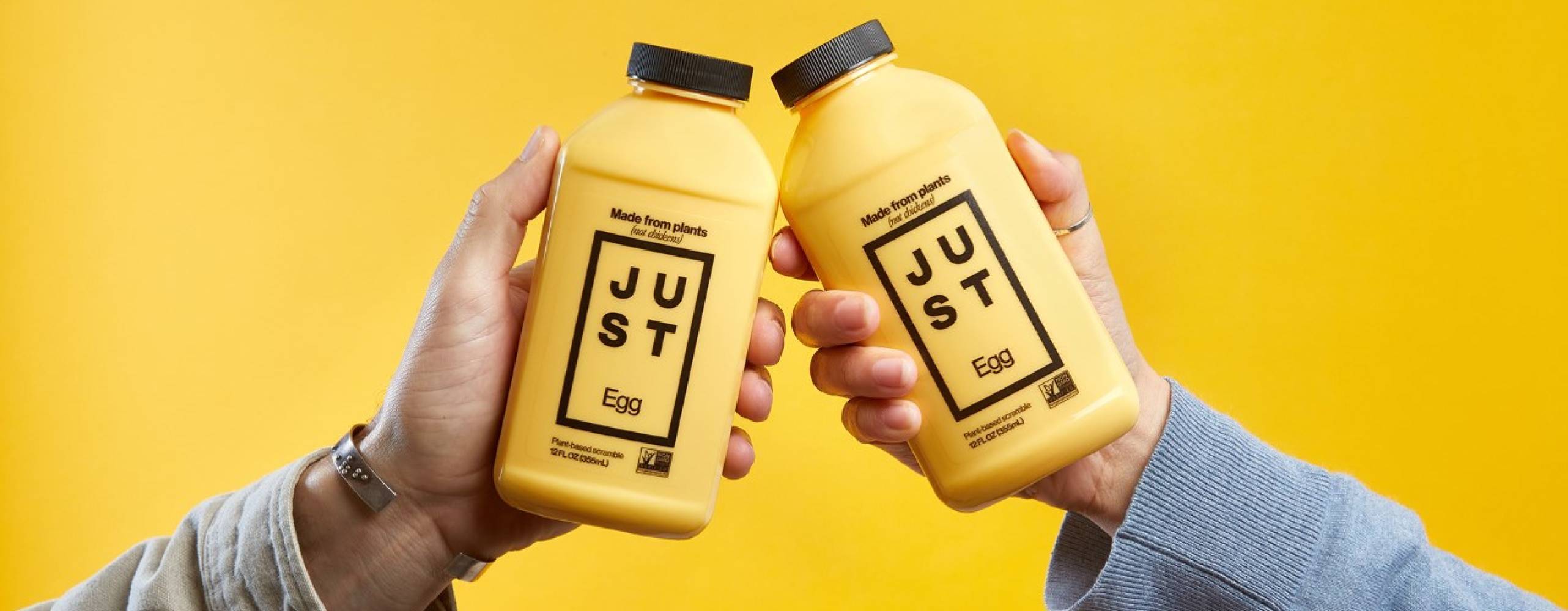 Två händer som håller upp en varsin plastflaska mot varandra mot en gul bakgrund.