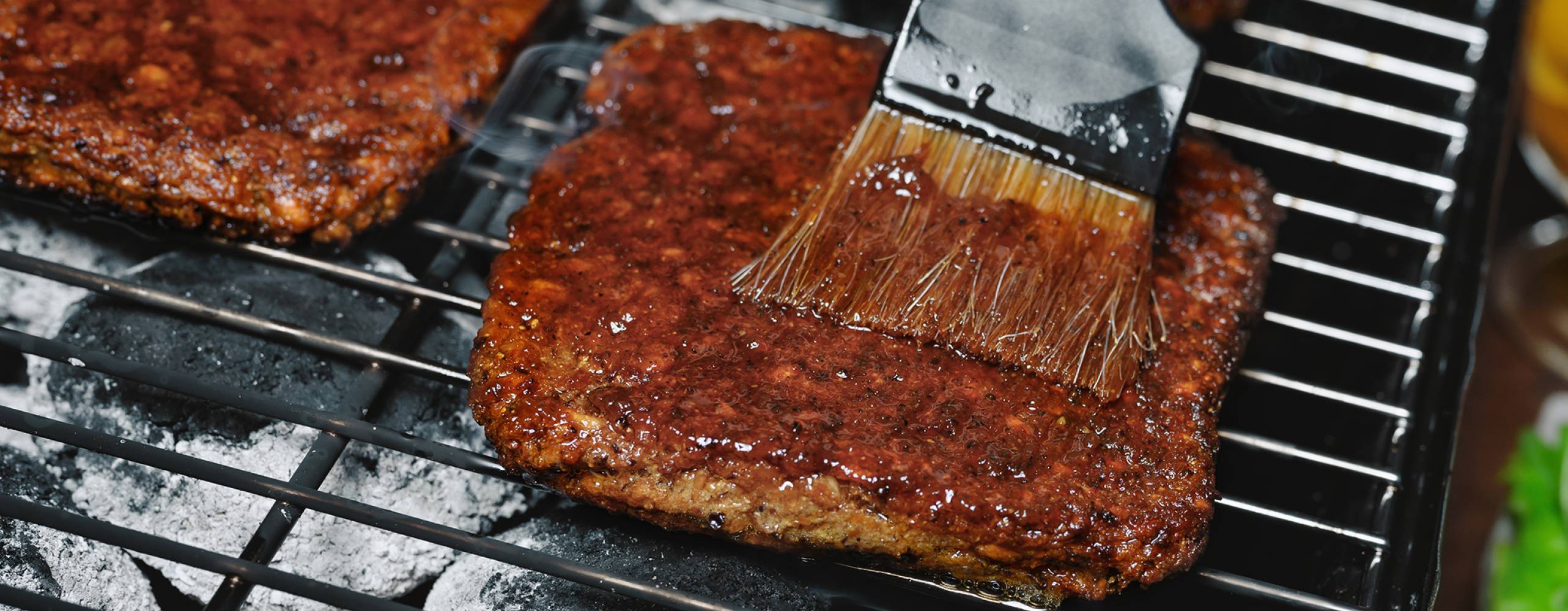 Fyrkantiga veganska burgare på en grill som blir penslad med grillolja.