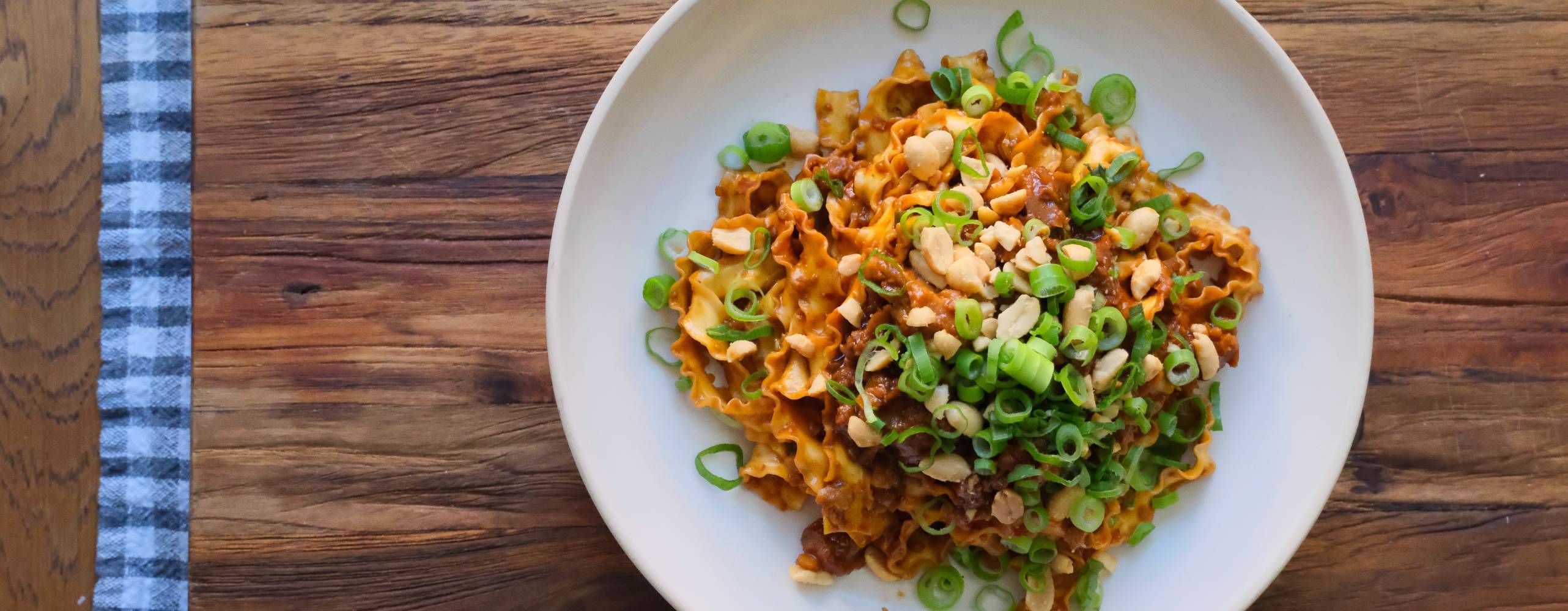 Veganska nudlar uppdukad på en vitt tallrik på ett träbord.