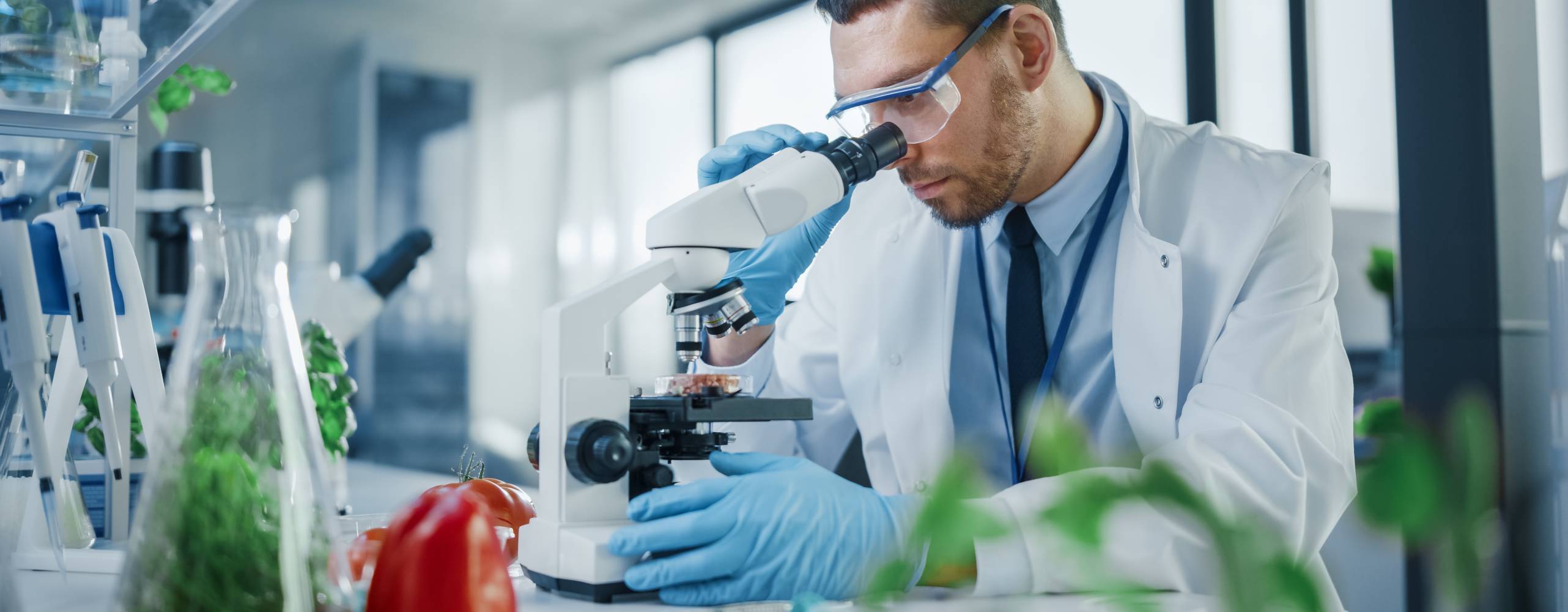 Man i vit labbrock undersöker något i ett mikroskop.