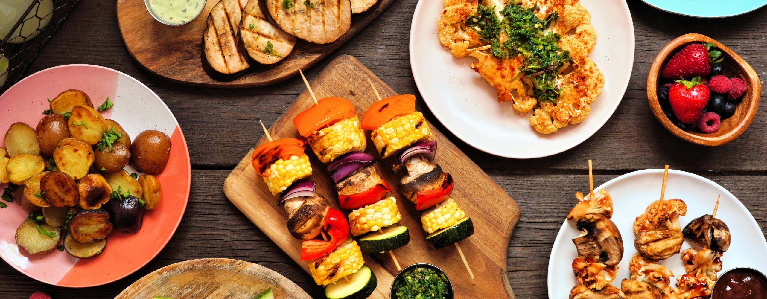 Växtbaserad grillbuffe med frukt och grönsaker mot ett mörkt träbord.