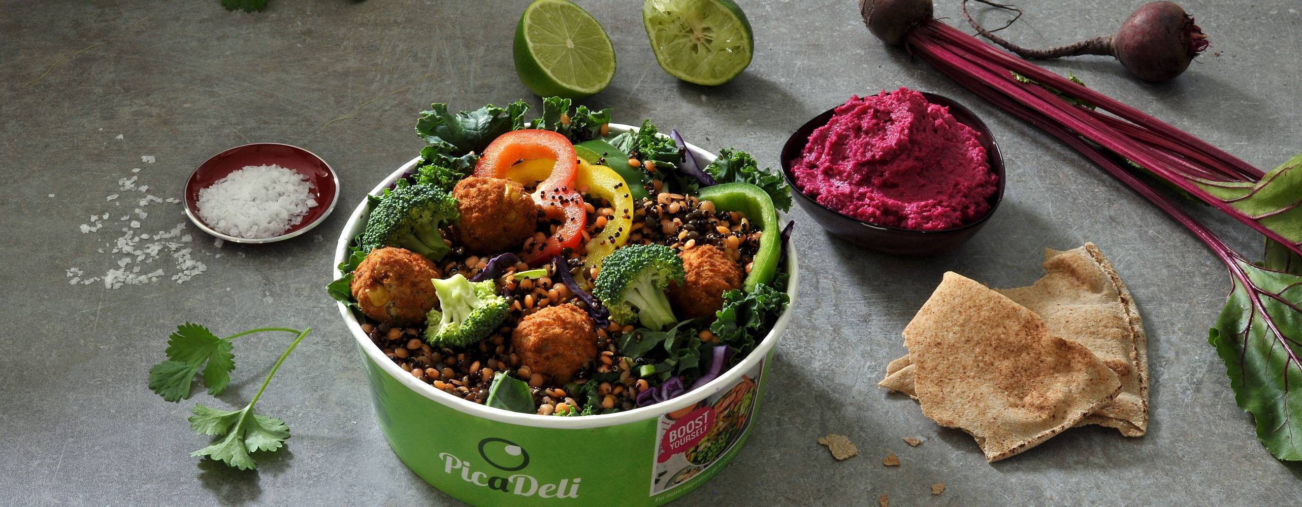 Växtbaserad sallad i en picadelibehållare med olika grönsaker utspridda runt om på ett granitgrått bord.