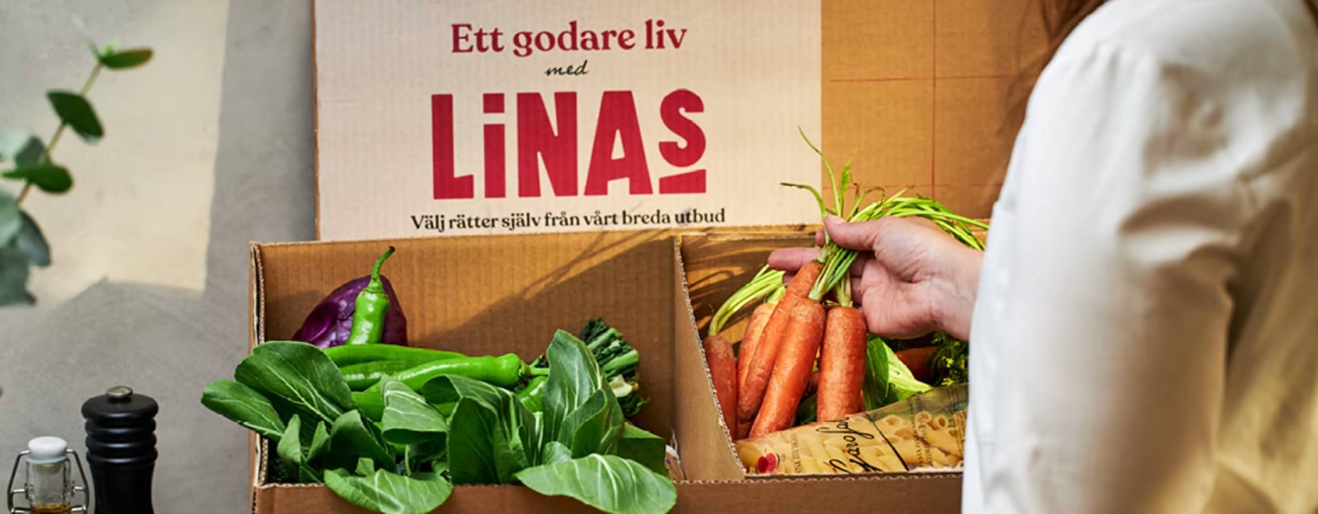 En kartong från Linas Matkasse med olika grönsaker och råvaror i.