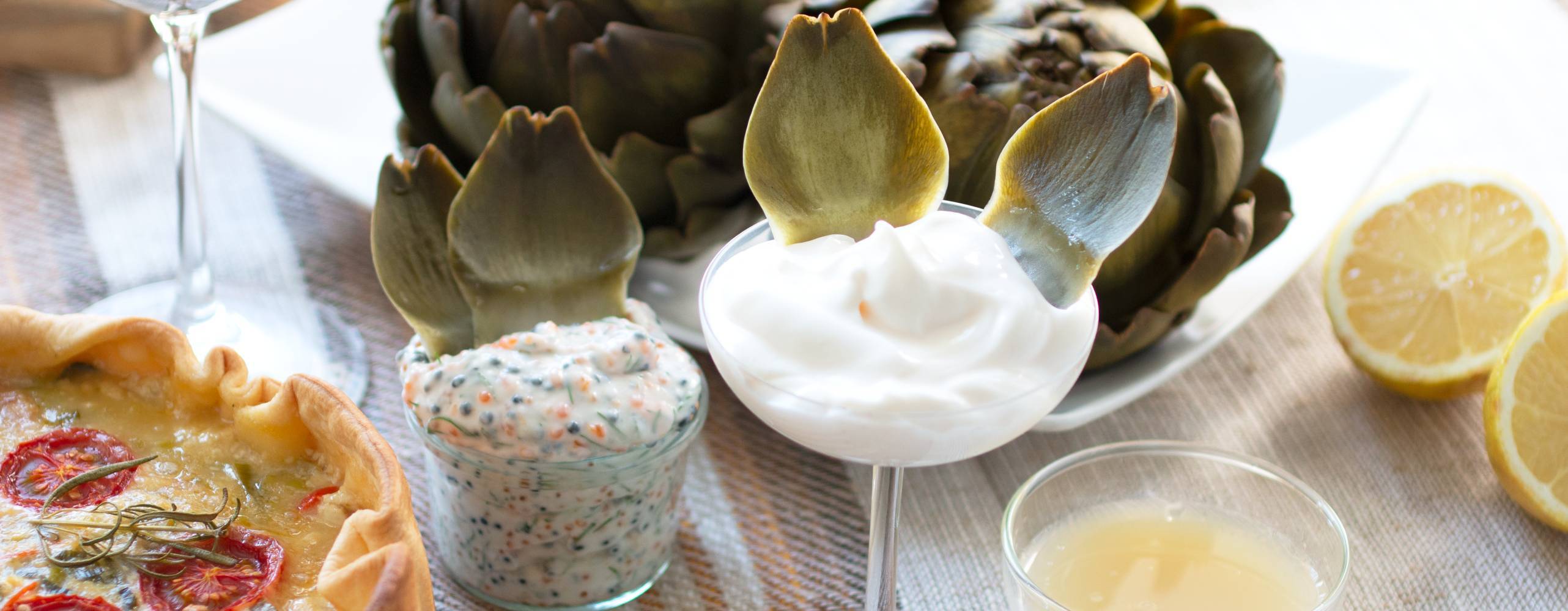 kokad kronärtskocka med tre olika dippar dukade på ett bord bredvid en paj