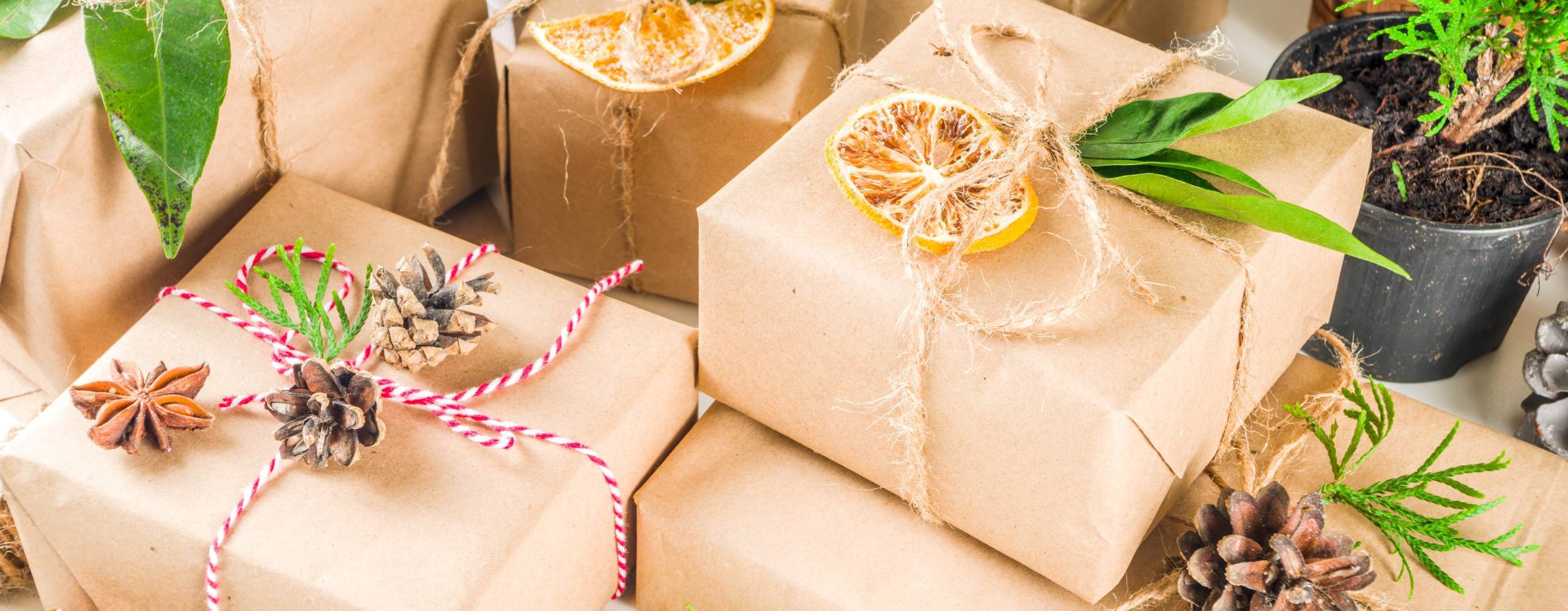 Presenter inslagna med brunt papper, apelsinskivor, hampasnören, kottar och grönt.