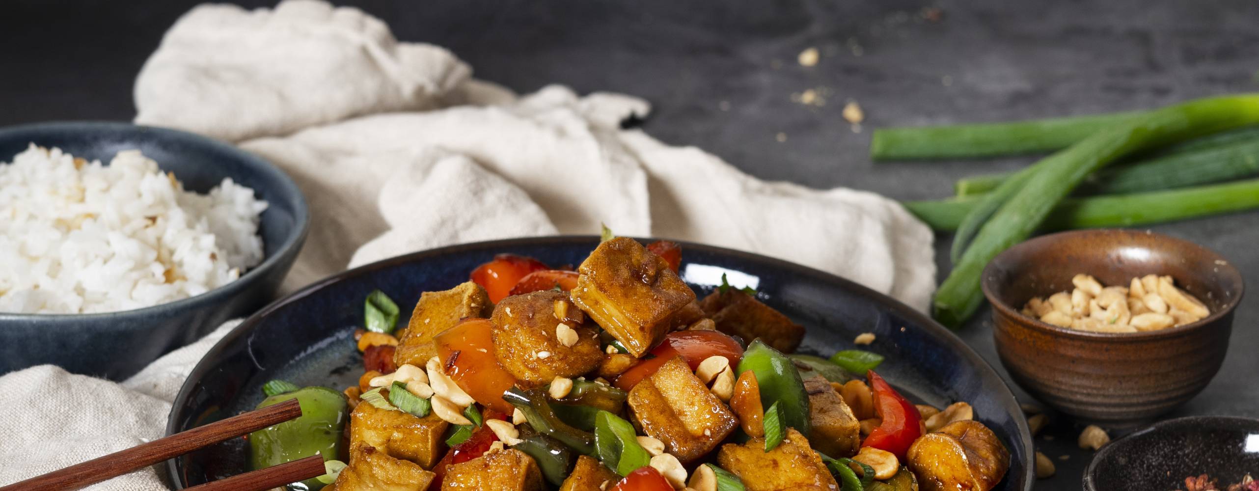 Kung Pao rätt i djuptallrik på en kökshandduk mot en mörkgrå bakgrund