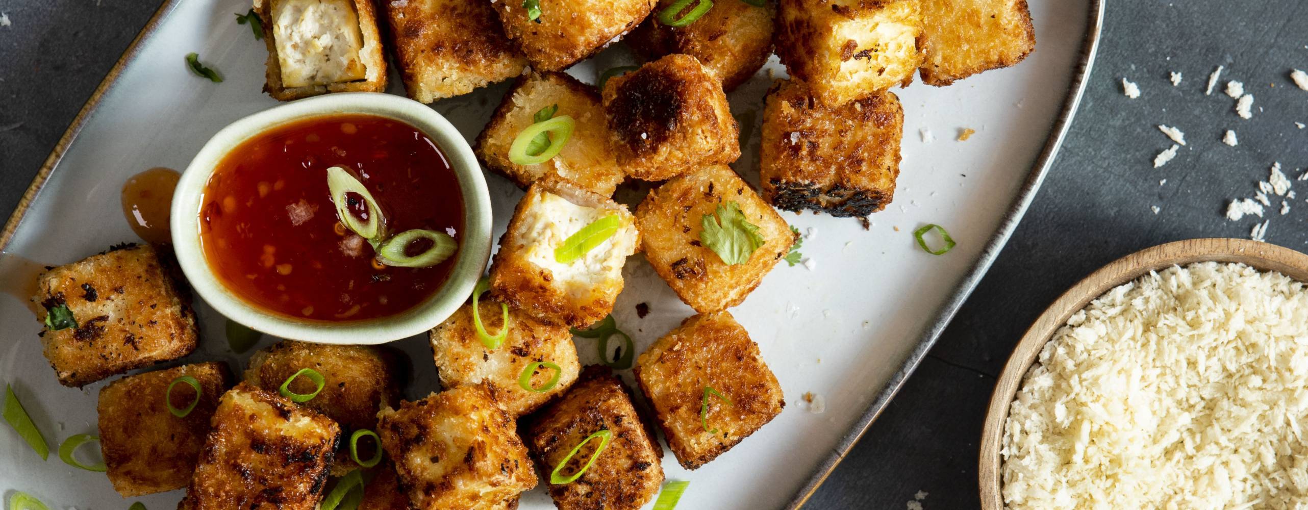 Panerad tofu på ett ljust serveringsfat mot en mörk bakgrund.
