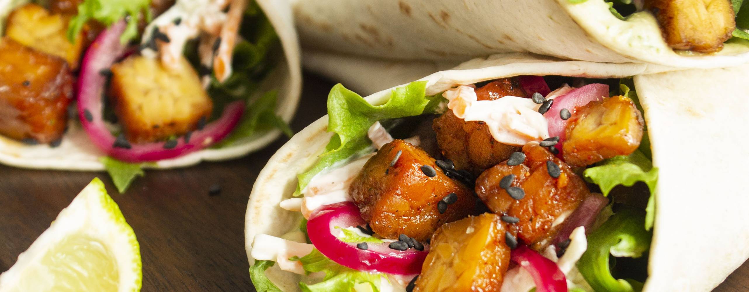 tre veganska wraps uppstaplade på en skärbräda i trä