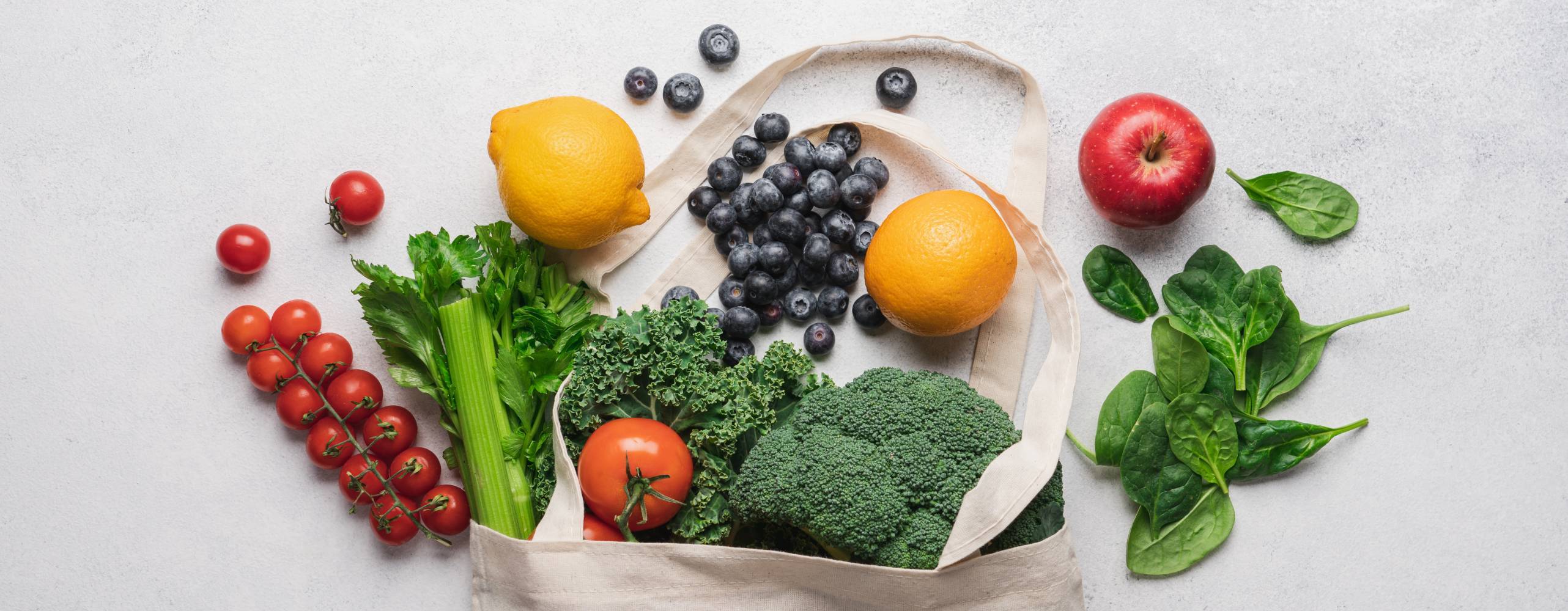 Handla hälsosam mat i bomullspåse med noll avfall. Selleri, grönkål, tomat, spenat, blåbär, broccoli, citron, apelsin ovanifrån