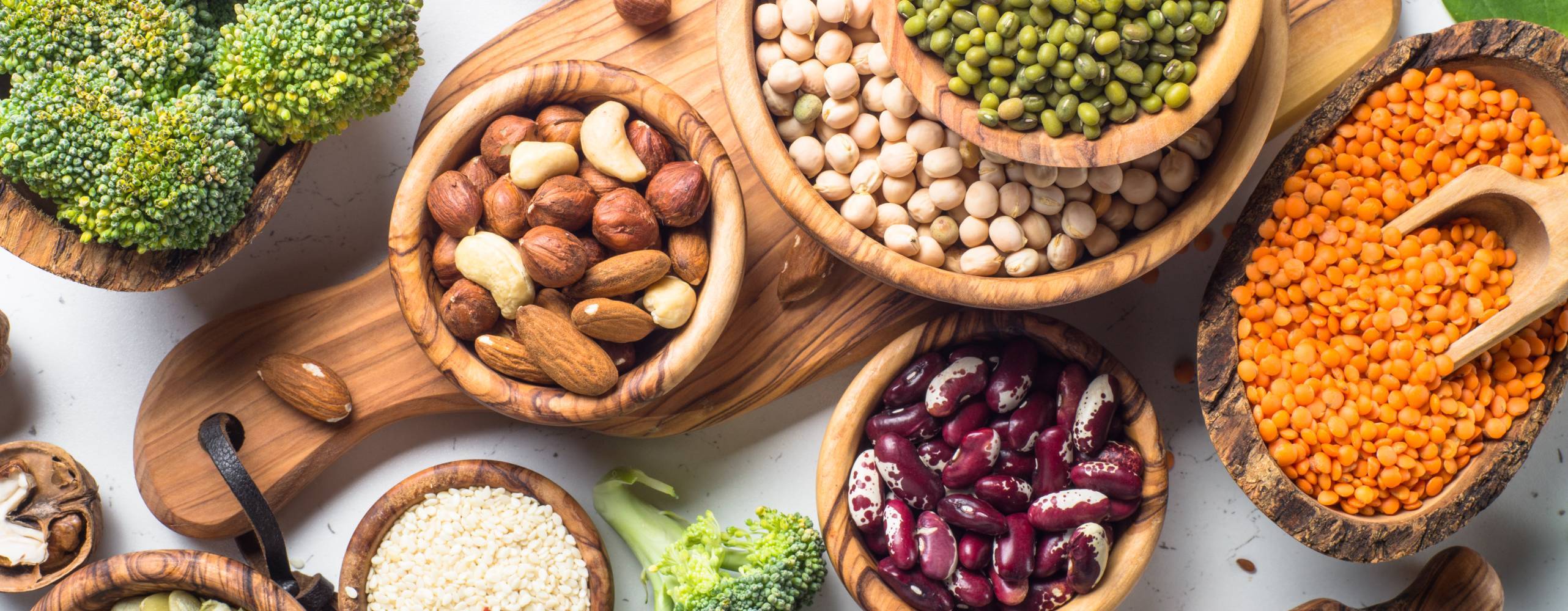 Vegansk proteinkälla. Bönor, linser, nötter, broccoli spenat och frön. Uppifrån på vitt bord.