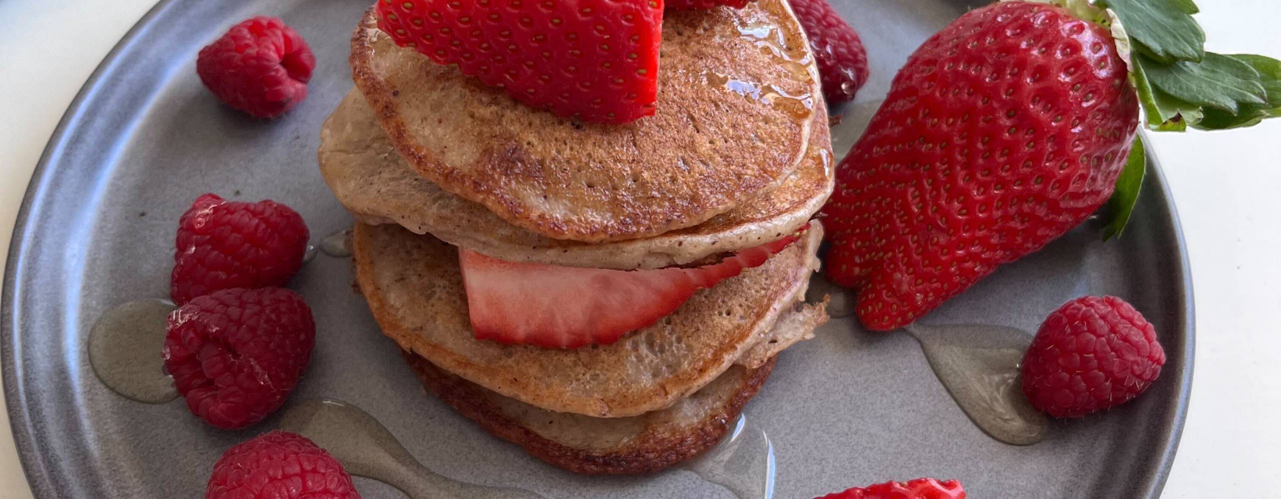 Amerikanska pannkakor staplade på ett grått fat med jordgubbar och hallon