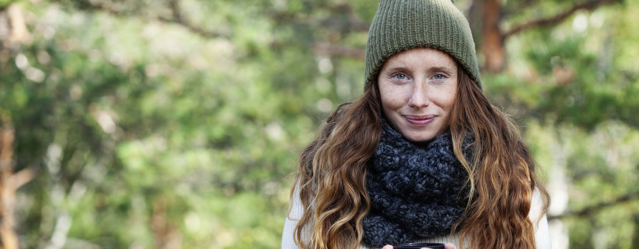 Kvinna ute i naturen med en kopp i sina händer.