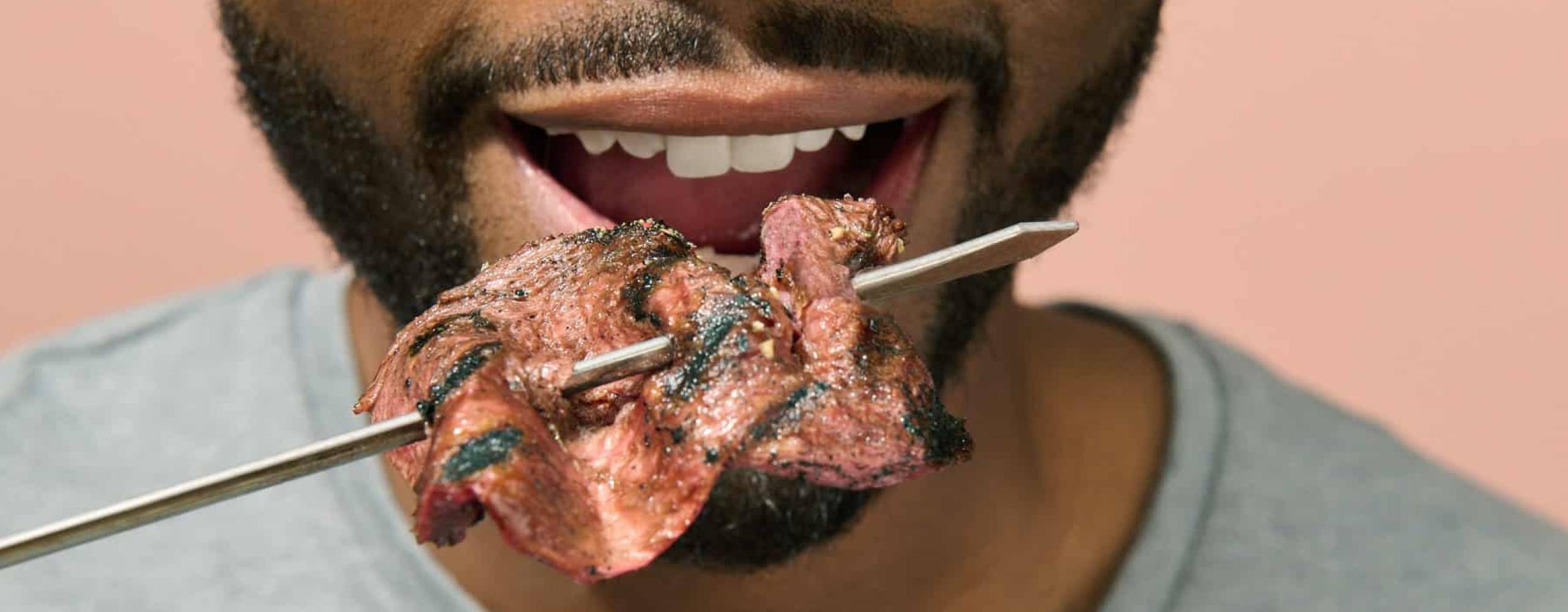Bild på en mans mun med ett grillspett med kött framför sig