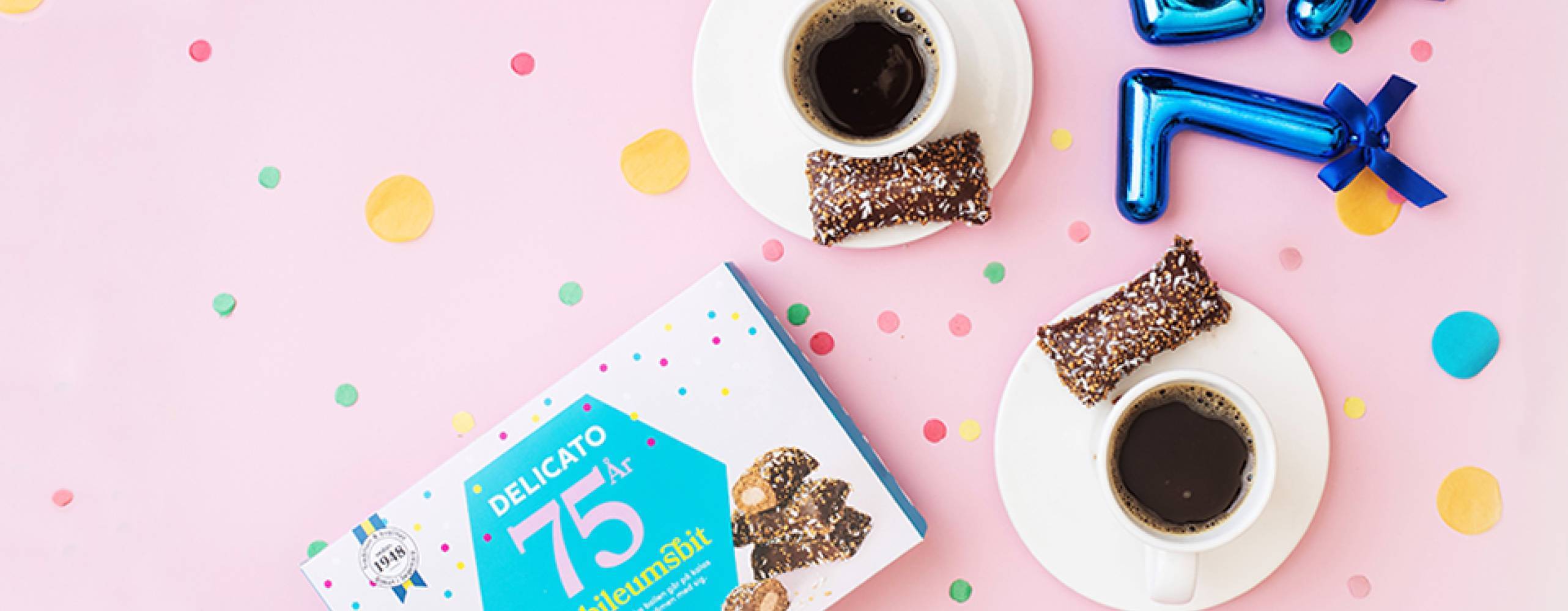 två koppar kaffe med en varsin kondisbit bredvid på ett ljusrosa bord