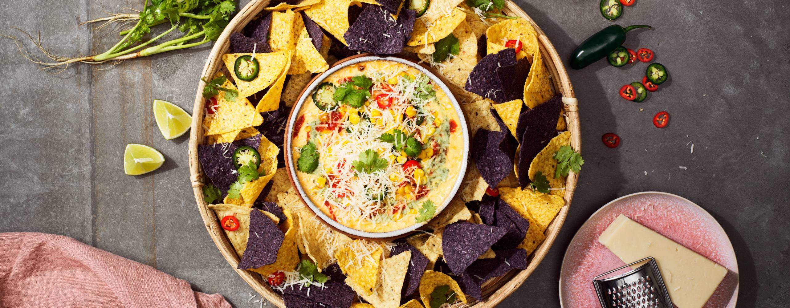 En skål med nachos och en liten skål med vegansk ostdipp mitt i den stora nachoskålen