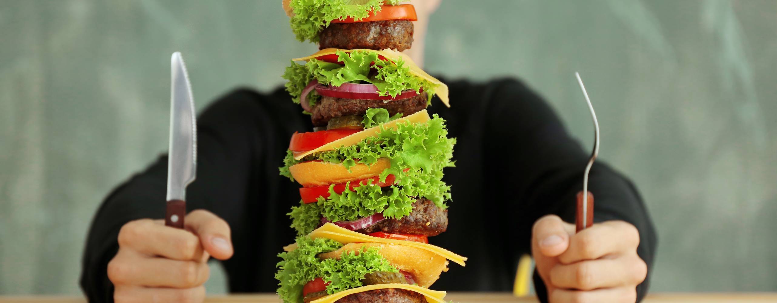 Man äter en stor hamburgare vid ett bord