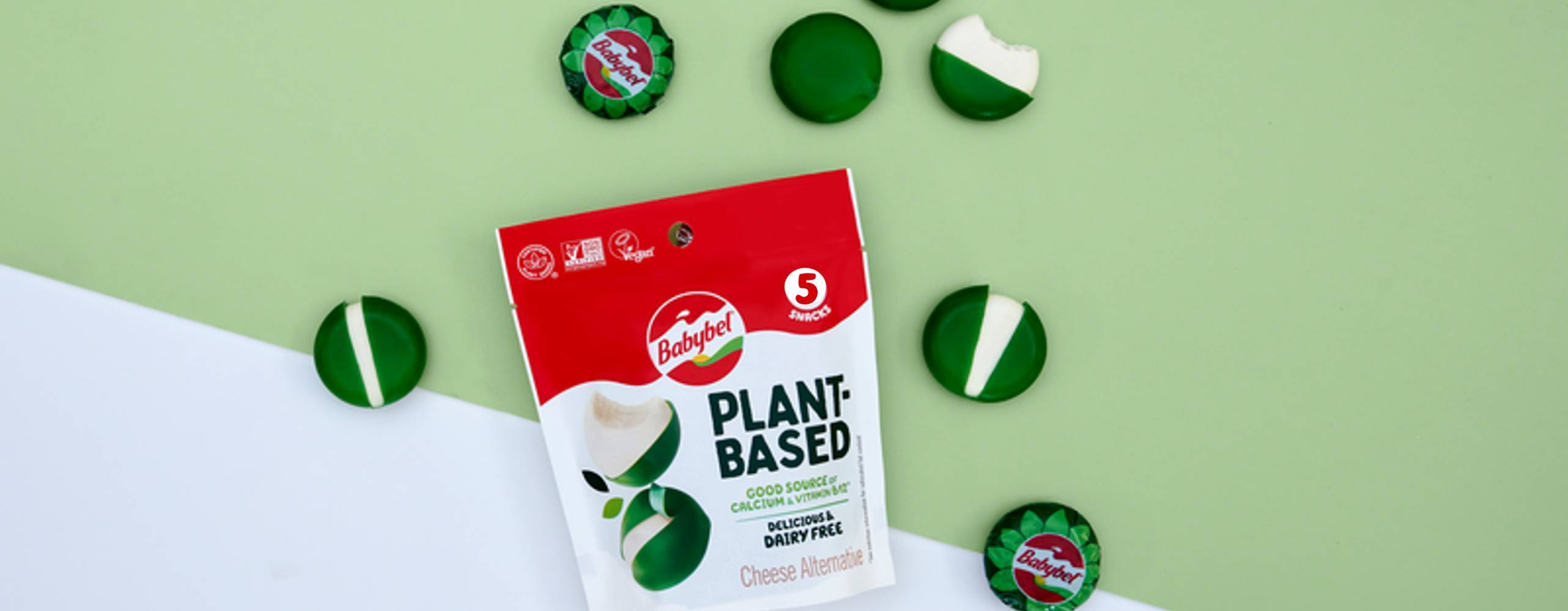 En förpackning växtbaserade ostar från Babybel på en grön och vit bakgrund, bild tagen uppifrån.