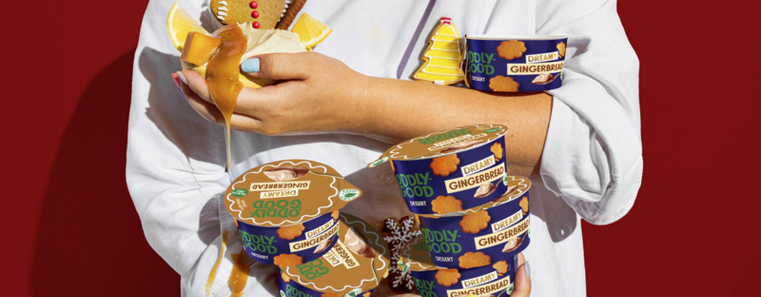 Person i vit tshirt mot en röd bakgrund som håller i flera burkar med packeterad dessert