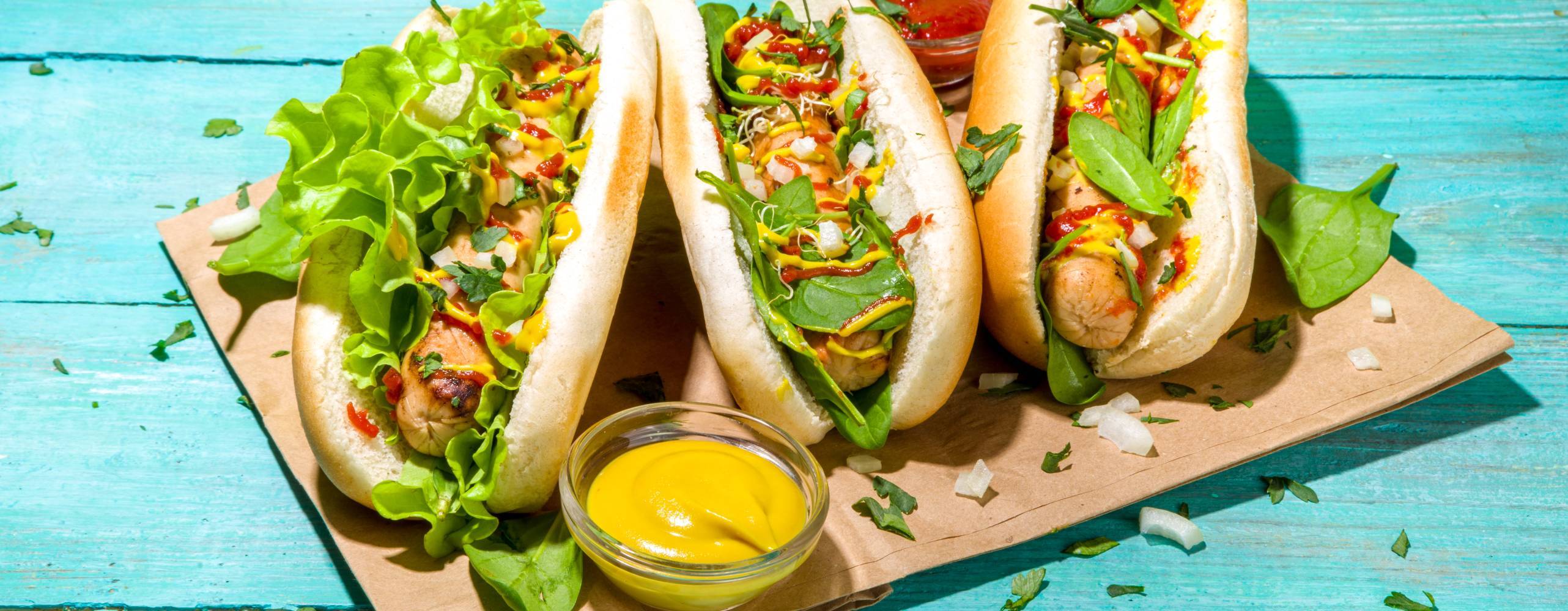 Tre veganska korv med bröd på ett bakplåtspapper på ett turkost träbord