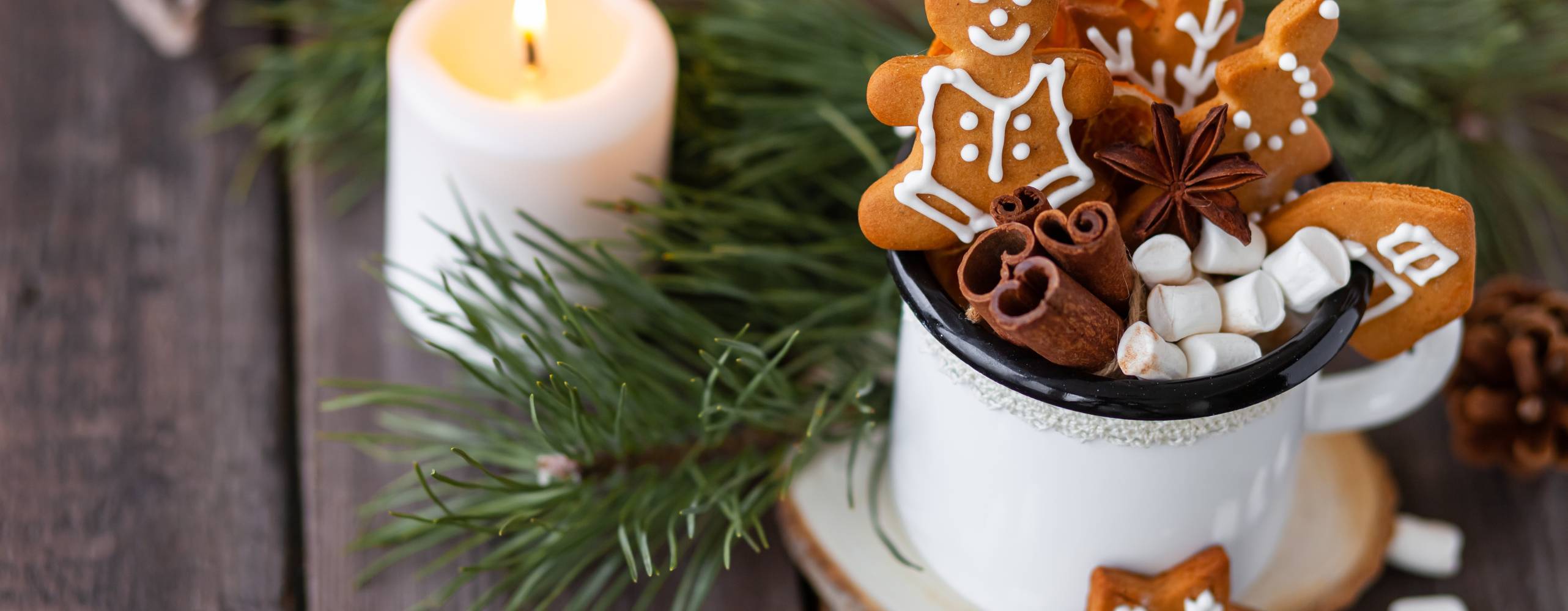 Hot winter drink in a white mug: cozy home composition with homemade gingerbread cookies, tree branch. Wooden background, christmas lights and candles