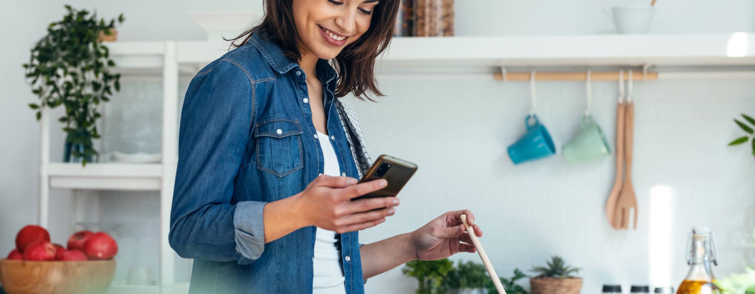 Shot of smiling beautiful woman using her mobile phone while cooking vegetables in the kitchen at home.