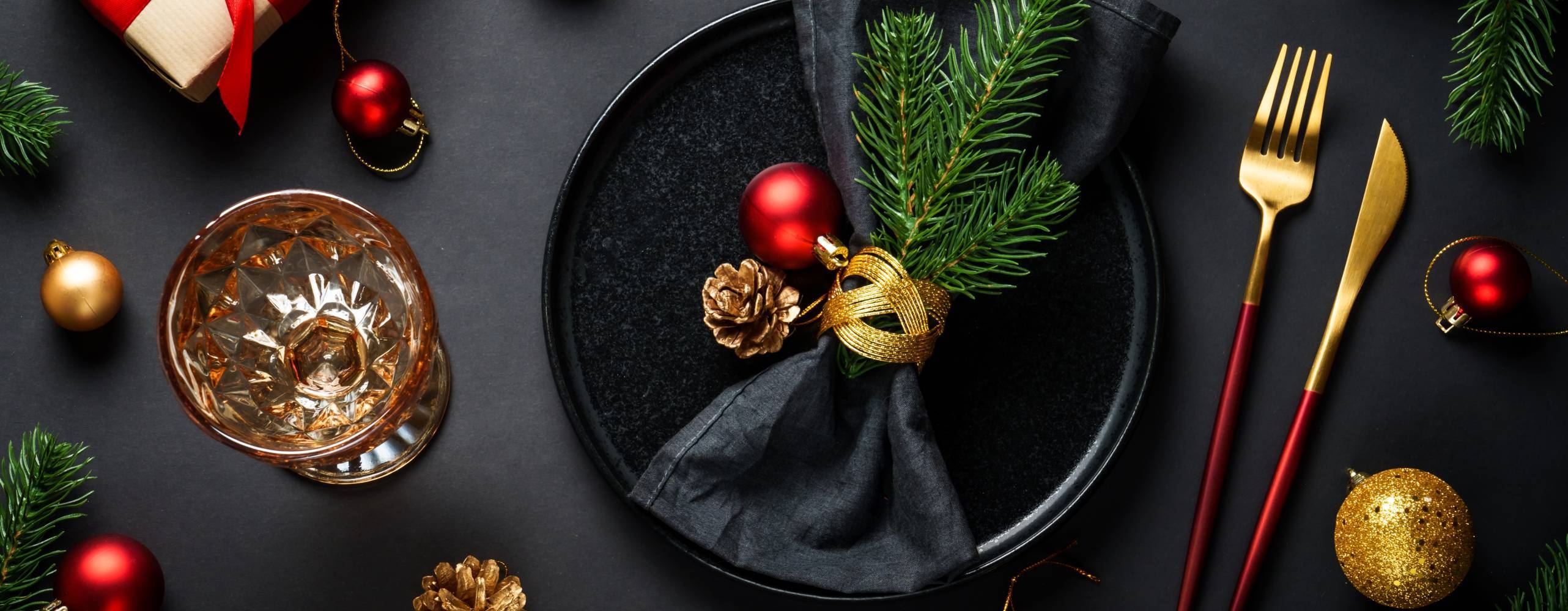 Christmas table setting with black plate, wine glass, cutlery and holidays decorations.
