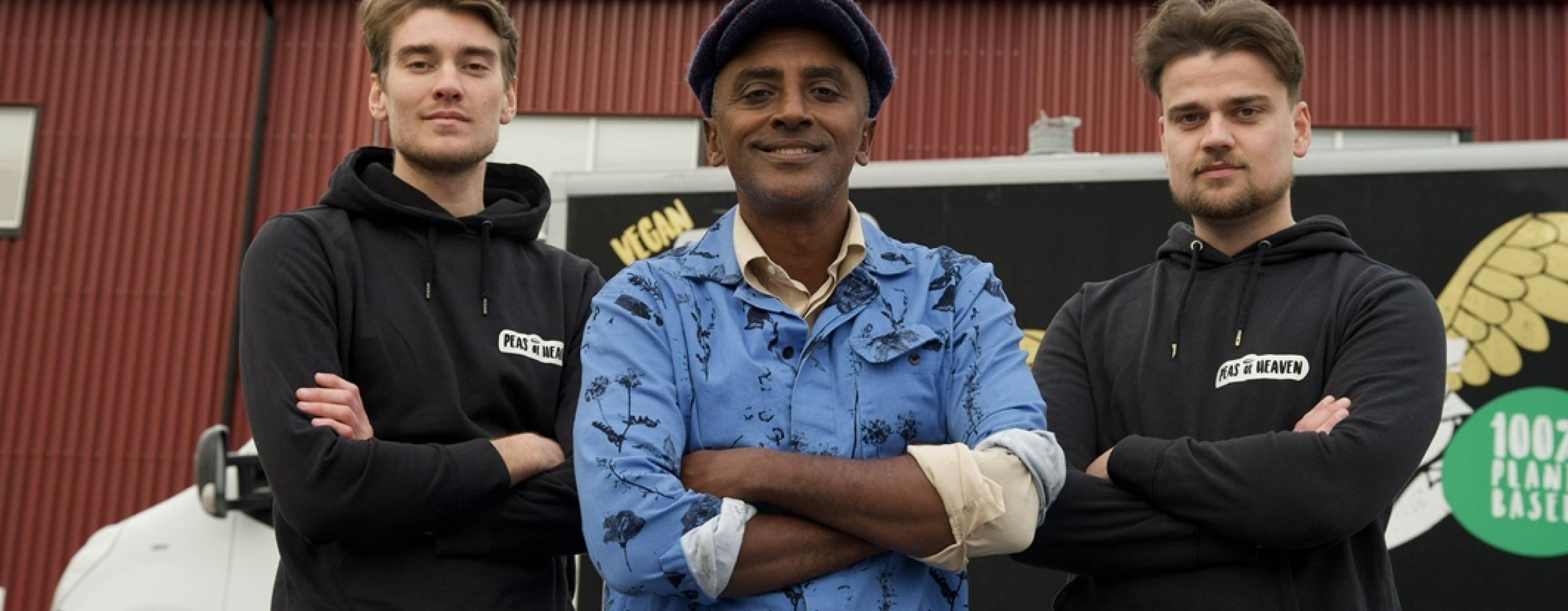 Tre män som står uppradade mot en röd vägg