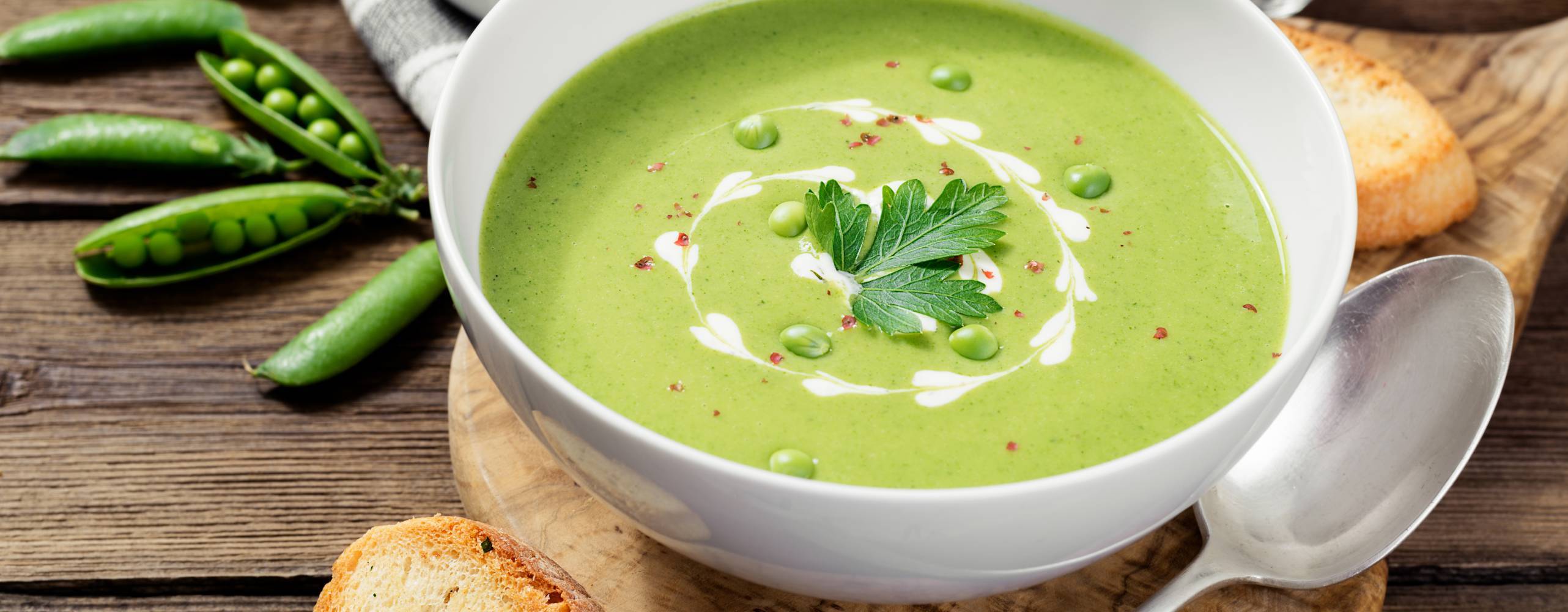 en skål med grön ärtsoppa på en underlägg i trä