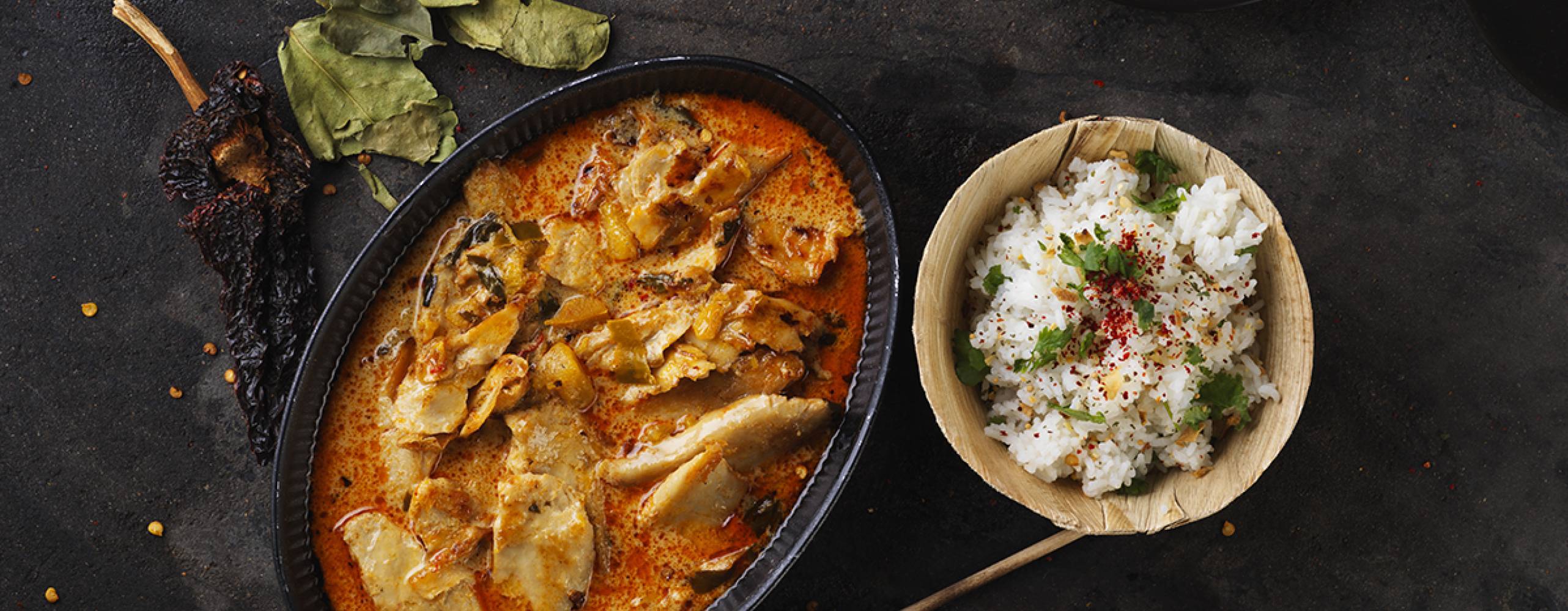 Vegansk röd curry i en gryta bredvid en skål ris på ett svart bord
