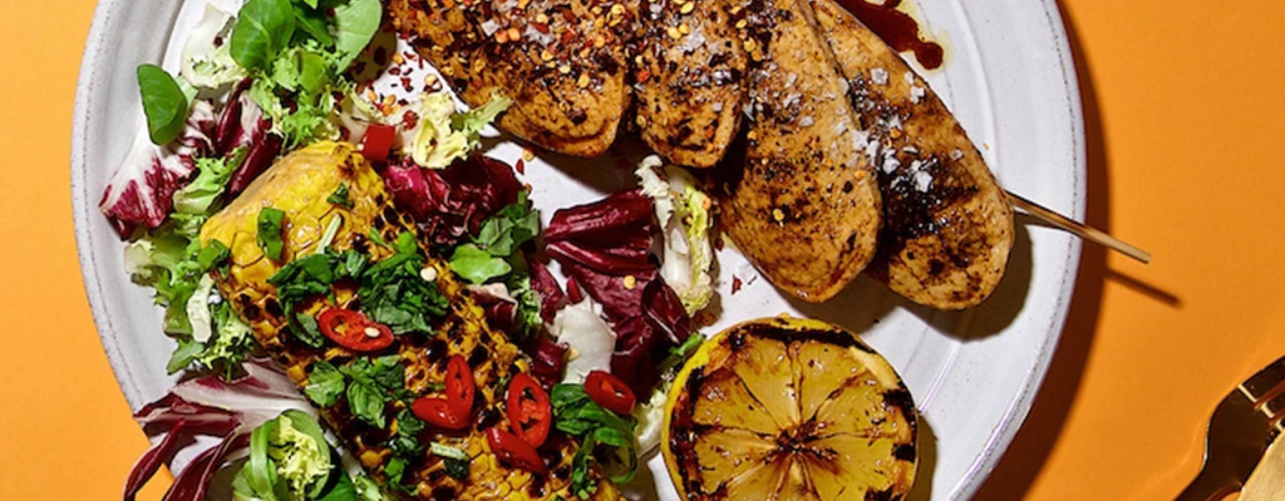 Vegofiléer med majskolv och grönsaker på en tallrik, på ett oranget bord.