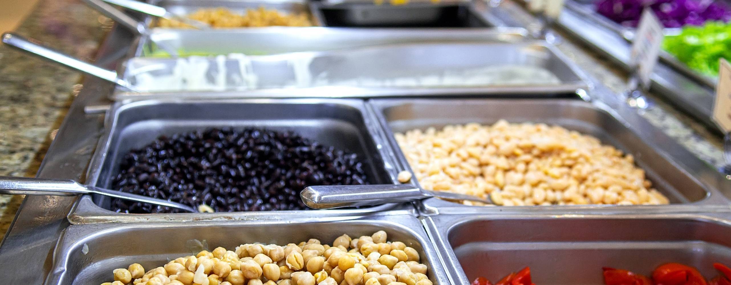 Självbetjäningsbuffé i restaurang, hotell eller café organiserad enligt smörgåsbordsprincipen. Rostfria skavningsrätter innehåller kokta vita bönor, cannellini-stil i övre brickan och svarta bönor, sköldpaddsbönor i nedre brickan