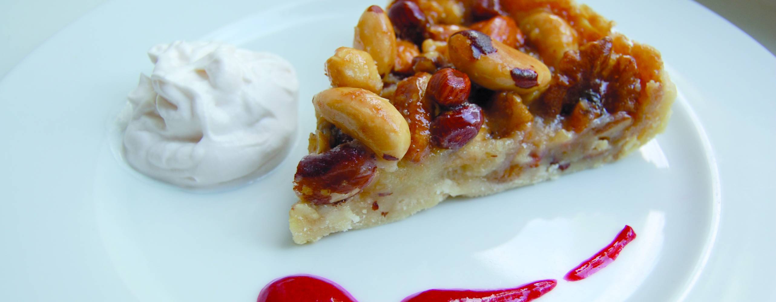 Vegansk nötpaj med vaniljgrädde och hallonsås på en vit tallrik
