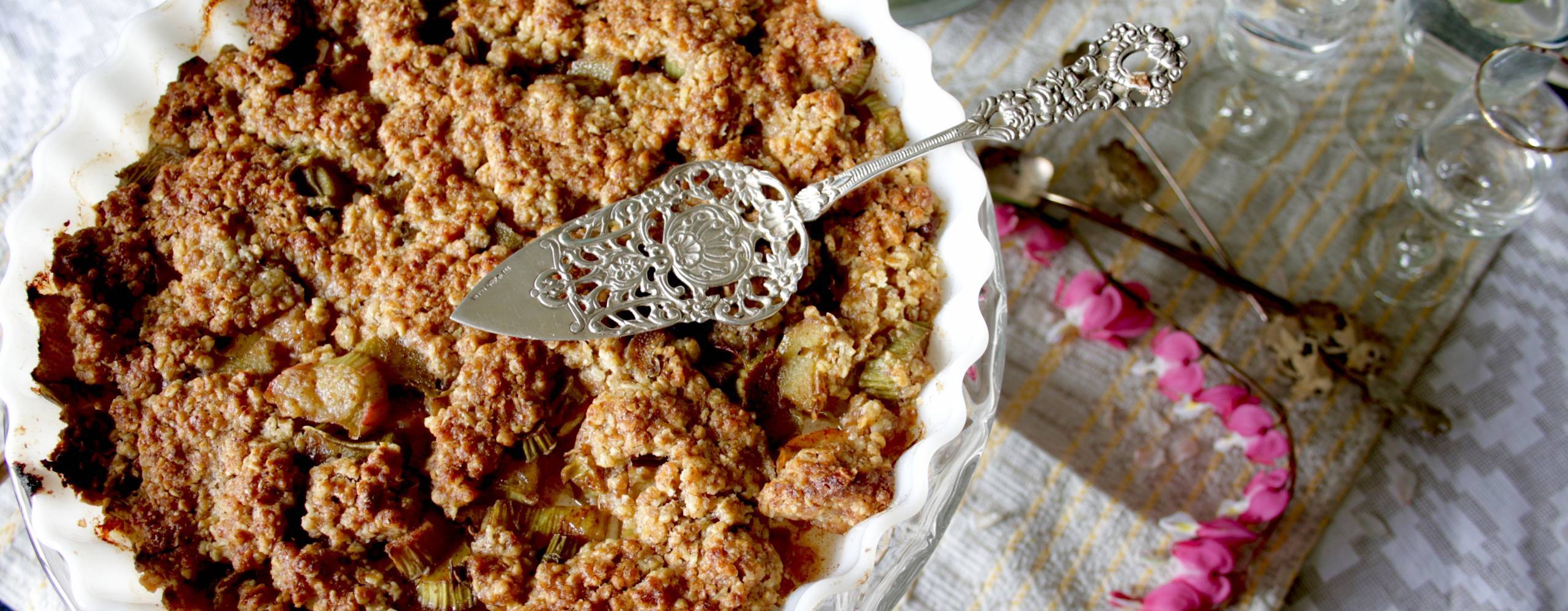 Rabarberpaj i en vit form på ett vit duk, bredvid ligger en rosa blomma.