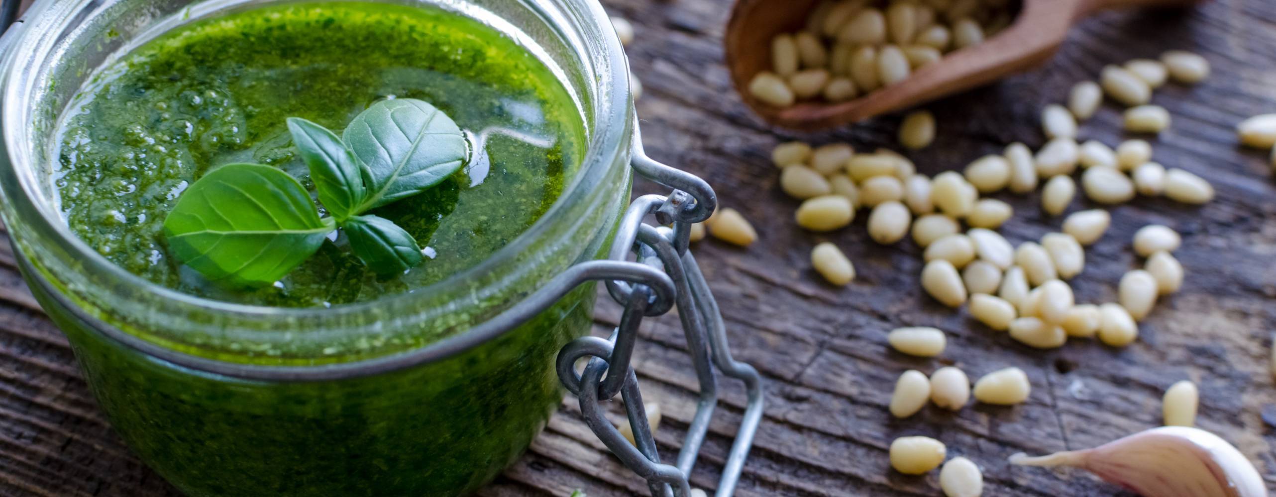 Bild på grönpesto på ett bord med utrströdda pinjenötter.