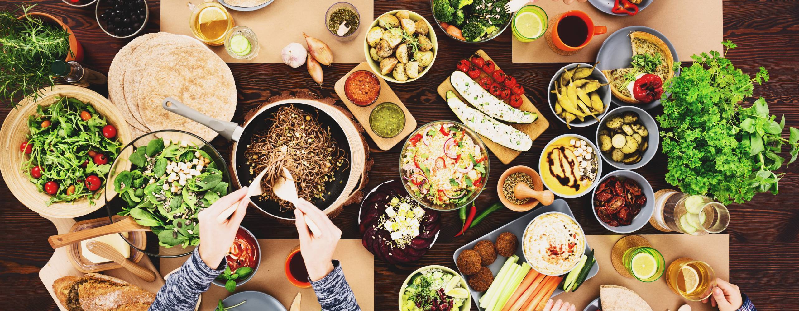 Bild på matbord taget ovanifrån där flera händer plockar vegansk mat